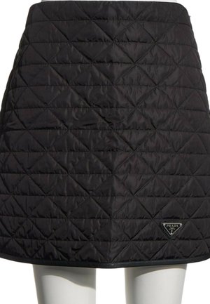 Jupe matelassée noire avec des motifs en losange et un petit logo Prada en bas à droite, portée sur un mannequin.