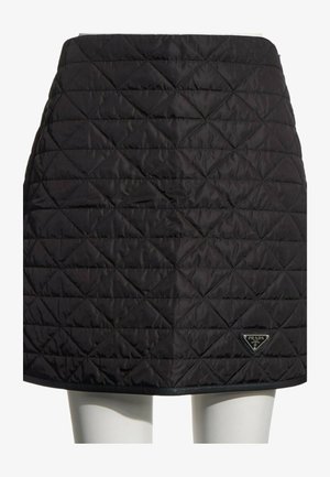 Jupe matelassée noire avec des motifs en losange et un petit logo Prada en bas à droite, portée sur un mannequin.