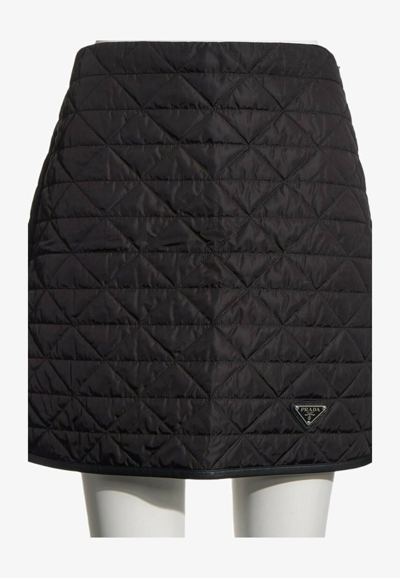 Jupe matelassée noire avec des motifs en losange et un petit logo Prada en bas à droite, portée sur un mannequin.