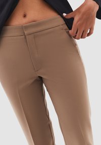 Beige op maat gemaakte broeken met een gladde textuur, voorzien van een rechte voorkant, zijzakken en een slanke pasvorm, gecombineerd met een donkere blazer.