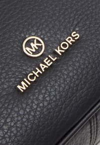Borsa a tracolla in pelle nera granulosa con logo circolare dorato MK e la scritta "MICHAEL KORS" in rilievo dorato sul davanti.