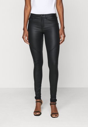 Slim-fit black faux leather pants with stitched knee details, worn with a white top and black strappy heeled sandals.