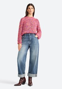 Rosa gestrickter Pullover mit strukturiertem Muster, kombiniert mit hellblauen, weit geschnittenen Jeans, die an den Knöcheln umgeschlagen sind, und braunen ankle boots mit Absatz.