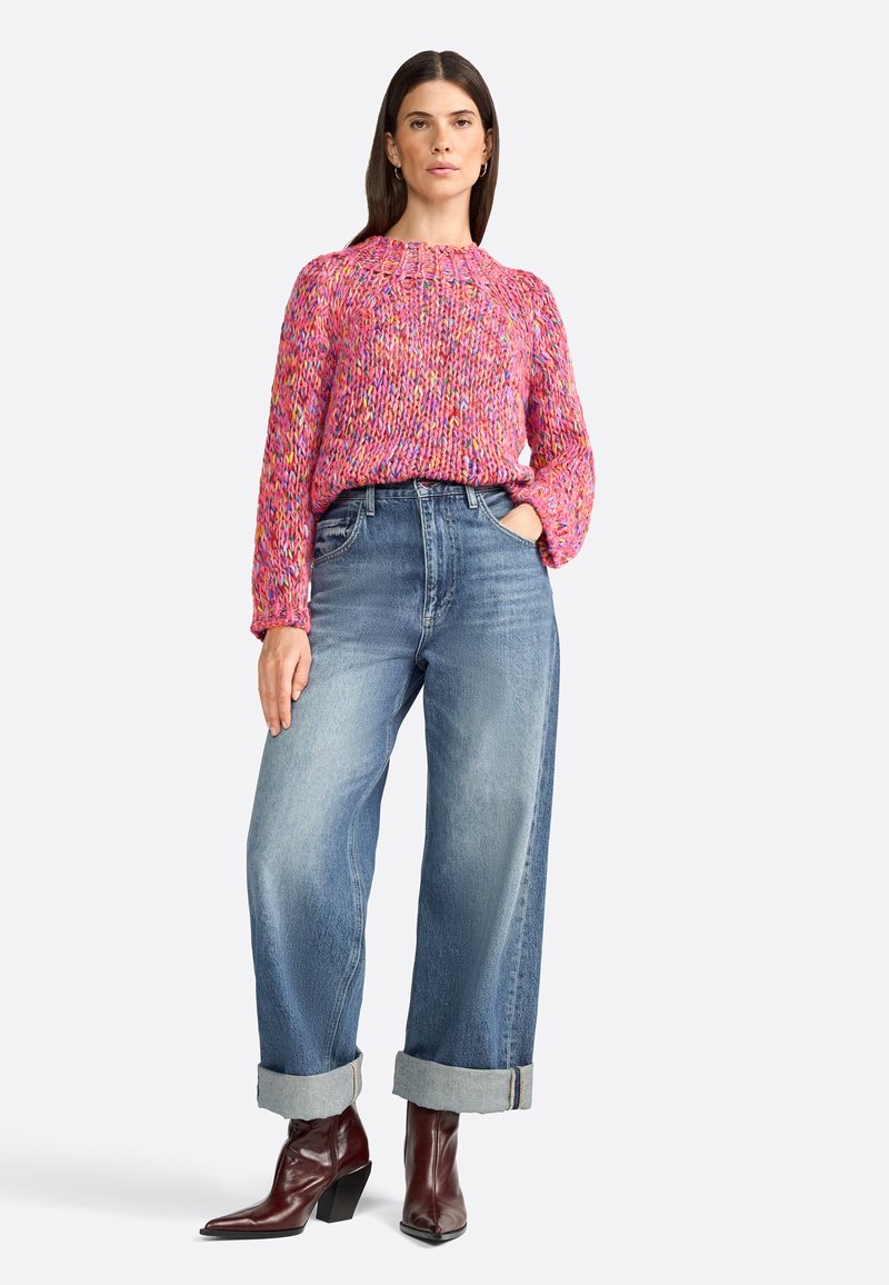 Rosa gestrickter Pullover mit strukturiertem Muster, kombiniert mit hellblauen, weit geschnittenen Jeans, die an den Knöcheln umgeschlagen sind, und braunen ankle boots mit Absatz.