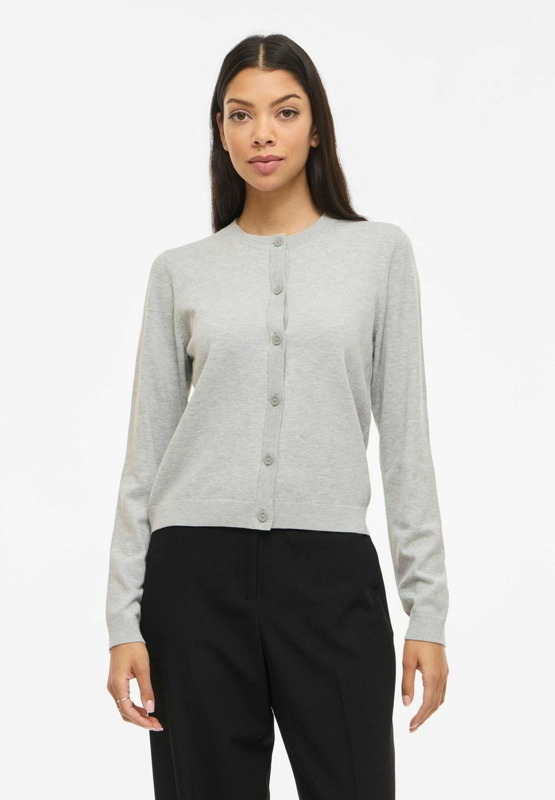Cardigan boutonné gris clair en maille douce, avec un col rond et des manches longues, présenté avec un ourlet court et des boutons en guise d'accents.