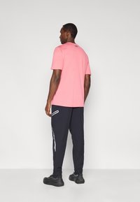 Ροζ μπλούζα κοντομάνικη με ριμπ υφή, συνδυασμένη με σκούρο μπλε παντελόνια που έχουν λευκές πλευρικές λεπτομέρειες. Μαύρα αθλητικά παπούτσια ολοκληρώνουν την εμφάνιση.