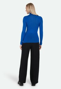 Royal blue długi rękaw golf wykonany z lekkiego materiału, dopasowany w talii, w połączeniu z szerokimi czarnymi spodniami i czarnymi botkami.