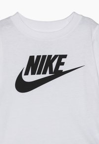 T-shirt bianca in cotone con un logo nero "NIKE" prominente e il design a swoosh. Scollo rotondo e maniche corte. Texture liscia.