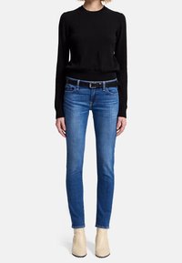 Black knit sweater, blue slim-fit jeans with belt, light-colored ankle boots. The outfit has a casual, fitted appearance.