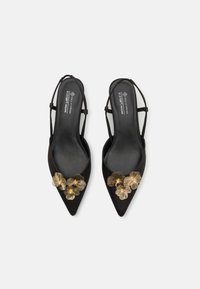 Chaussures slingback véganes noires à bout pointu, ornées de trois accents floraux métalliques dorés sur la zone des orteils et de fines brides autour de la cheville.