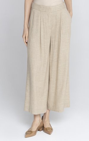 Kobieta nosząca beżowe spodnie o szerokich nogawkach z zakładkami, zestawione z cielistymi, niskimi szpilkami z ozdobą w postaci złotej klamry.