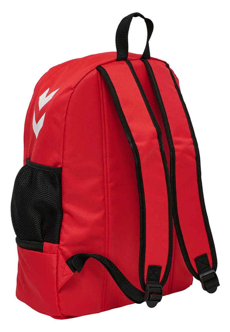 Mochila de tela roja con correas negras, bolsillo con cremallera y compartimento lateral de malla. Presenta un diseño de logo en chevron blanco en el frente.