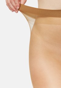 Gennemsigtige nylonstrømpebukser strækkes, med en brun talje og en lys beige ben. Glat tekstur med en let glans.