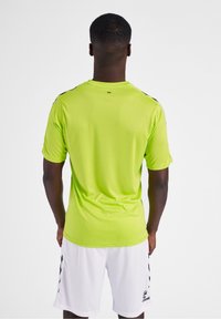 Camiseta deportiva de manga corta en verde fluorescente, hecha de tejido ligero, con detalles en negro en los hombros y un cuello redondo.