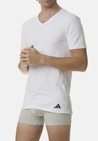 Witte katoenen V-hals T-shirt, korte mouwen, met een klein zwart Adidas-logo op de linker onderkant. Gecombineerd met grijze boxershorts.