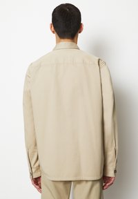 Light beige long-sleeve shirt made of smooth fabric, featuring a relaxed fit, button cuffs, and a back yoke design.