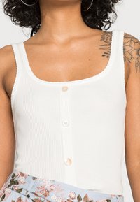 Top in cotone bianco a coste con spalline larghe, scollo quadrato e tre bottoni in perla sul davanti. Presenta un tessuto testurizzato.