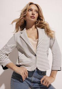 Wzorzysta marynarka w kolorze kremowym i granatowym, z rękawami 3/4, zapięciem na guziki i bocznymi kieszeniami, zestawiona z jasnoniebieskimi dżinsami o wysokim stanie.