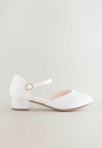 Pantofi albi cu vârful închis, cu un toc mic și pătrat și o curea subțire la gleznă, având o cataramă rotundă, decorată cu strasuri. Textură de material neted.