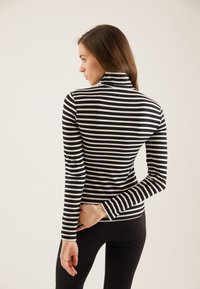 Svart- og hvitstripet turtleneck-genser med lange ermer, tettsittende design, laget av elastisk stoff, med høyt krage og glatt tekstur.