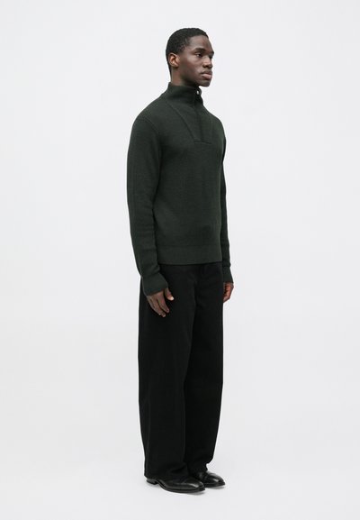 Σκοτεινό πράσινο πλεκτό πουλόβερ με ψηλό γιακά και μισή φερμουάρ. Συνδυασμένο με άνετα μαύρα παντελόνια και μαύρα επίπεδα παπούτσια. Απλός, υφασμένος σχεδιασμός.