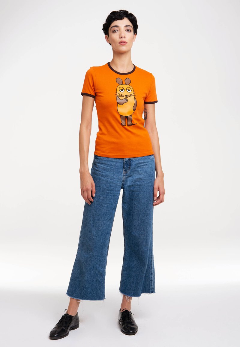 Orange T-shirt with brown-trimmed neckline and sleeves, featuring a cartoon character graphic. Paired with blue wide-leg jeans and black shoes.
