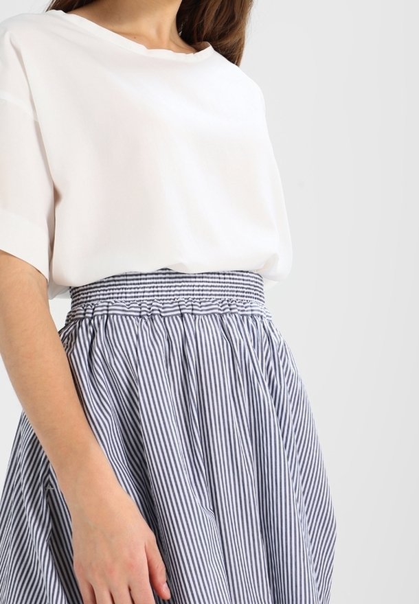Biała bluzka o luźnym kroju i krótkich rękawach, w połączeniu z niebieską spódnicą w paski, z elastycznym pasem i marszczoną fakturą.