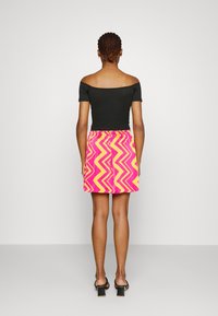 Off-the-shoulder black top paired with a brightly colored zigzag-patterned skirt in pink and yellow, featuring an elastic waistband.