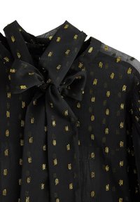 Sort bluse med en sløjfe ved halsen, prydet med guldmetallic prikker og en gennemsigtig stofstruktur.