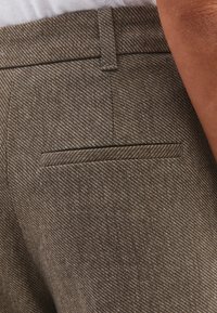 Hnědé kalhoty se vzorem a diagonálním pruhovaným designem. Mají jednu zadní kapsu a plochý pas pro upravený vzhled.