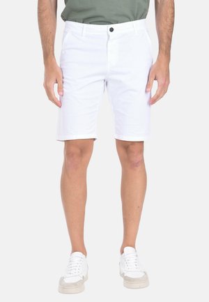 Pantaloni corti bianchi a taglio dritto, realizzati in un tessuto leggero, dotati di tasche laterali e chiusura a bottone. Abbinati a sneaker bianche.