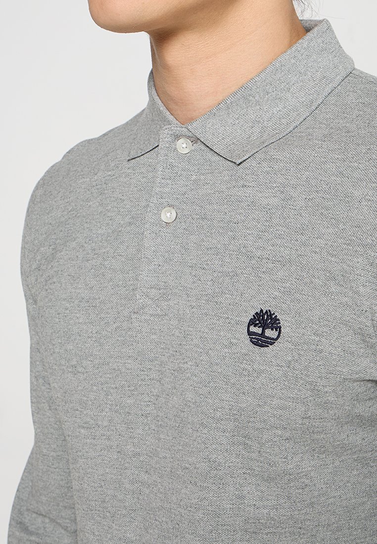 Polo gris en tissu texturé, avec un col à boutons et un logo d'arbre bleu marine sur la poitrine. Conception à coupe classique.