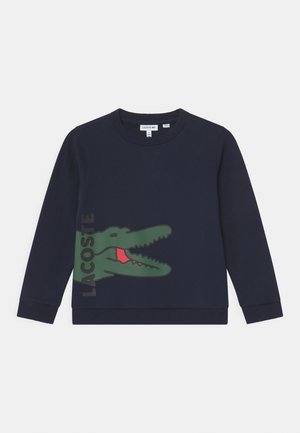 Sweatshirt bleu marine à col rond, avec des poignets et un ourlet côtelés. Présente un grand logo de crocodile vert avec des détails rouges à l'avant.
