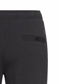 Zwarte sportbroek met een zachte textuur, elastiche tailleband en een diagonale ritszak op de rug met een ronde knoopsluiting.