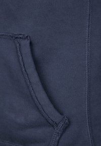 Sudadera de color azul marino con costuras visibles, presenta un detalle de bolsillo en el lado izquierdo, textura suave y aspecto de mezcla de algodón.