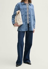 Lysblå denimjakke med forlommer og knappelukning, parret med mørkeblå flared jeans og en cremefarvet taske. Stribet top synlig.