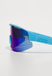 Blå sportssolglasögon med wrap-around design, utrustade med gradient linser i lila till blå och texturerade öronstöd med "bliz"-logotyp.