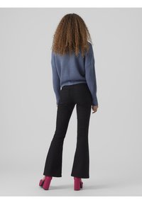 Blå stickad tröja med neddragna axlar, i kombination med högmidjade svarta utsvängda jeans. Modellen bär rosa kraftiga klackskor.