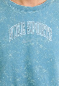 Ljusblå bomulls-T-shirt med en blekt textur. Har en vit broderad "NIKE SPORTS"-logotyp i en bågformad stil.