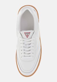 Witte sneaker met een glad leren bovenwerk, contrasterende bruine rubberen zool en een rood driehoekig logo op de tong. Vetersluiting.