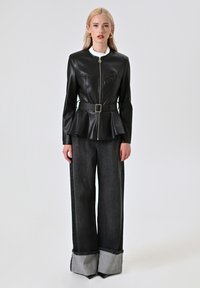 Giacca in ecopelle nera con chiusura a zip, vita a peplum e dettaglio con cintura. Abbinata a pantaloni in denim scuro a gamba larga con orli risvoltati.