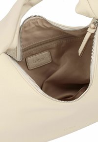 Interno di una borsa in pelle beige con un compartimento con cerniera, texture liscia e un'etichetta logo discreta. Foderato con tessuto chiaro.