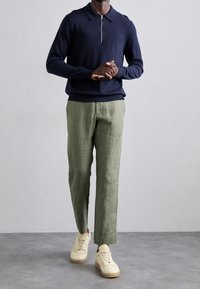 Marinblå dragkedja i stickad polo, ljusgröna linbyxor och beige sneakers. Slät textur, klassisk krage, skräddarsydd passform och kontrasterande detaljer.