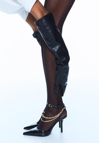 Črne usnjene rokavice do stegen v kombinaciji s črnimi čevlji z ostro konico, ki imajo zlato verižico, ter črnimi prosojnimi nogavicami. Povsod gladka tekstura.