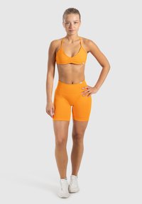 Sujetador deportivo naranja con tirantes ajustables, combinado con pantalones cortos de ciclismo naranja de cintura alta, hechos de una tela ligera y elástica.