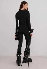 Top negro de manga larga y leggings con un diseño ajustado. Botas de esquí negras con hebillas y bastones de trekking negros. Tela suave y elástica.