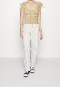 Beige nařasený top s balónovými rukávy a zavazováním vpředu, ve spojení s bílými širokými kalhotami a černými teniskami s bílou podrážkou.