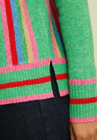 Krāsains adīts džemperis ar zaļo bāzi un vertikālām svītrām rozā, zila, sarkana un brūna krāsā; ribota apakšmala ar sānu šķirtni.