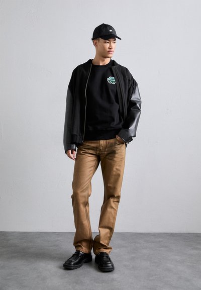 Musta pommikindel jakk nahkvarrukatega, must graafika sweatshirt, pruunid püksid ja mustad kingad paksude talladega. Peas lihtne müts.