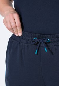 Navy siniset joustavat housut, joissa on nauhakuja turkooseilla päihin; kangas on sileä ja suunniteltu mukavuutta varten.